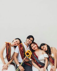 a group of people sitting next to each other on top of a white couch holding sunflowers