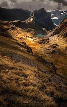 the mountains are covered in brown grass and some green water under a dark sky with clouds