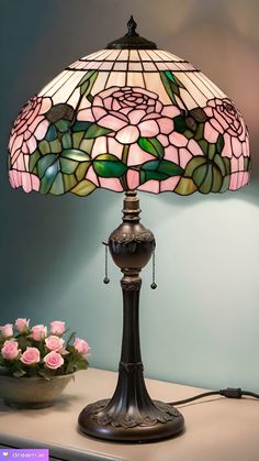 a table lamp sitting on top of a desk next to a vase with flowers in it