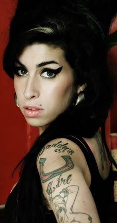 a woman with black hair and tattoos on her arm posing for a photo in front of a red wall