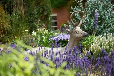 a deer statue sitting in the middle of a garden filled with purple and white flowers