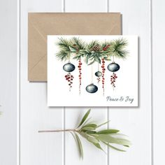 a christmas card with pine cones and baubles hanging from the branches on top of it