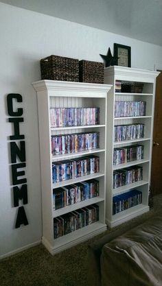 a white bookcase with several movies on it in a room next to a bed