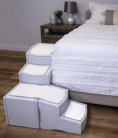 a white bed with four step stools next to it on a wooden floor in a bedroom