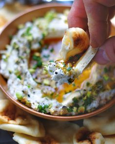 a hand dipping an egg into a bowl filled with tortilla shells and garnished with parsley