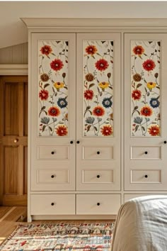 a bed sitting next to a white cabinet with flowers painted on the doors and drawers