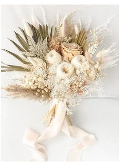 a bridal bouquet with dried flowers and feathers on white fabric, ready to be used as a wedding bouquet