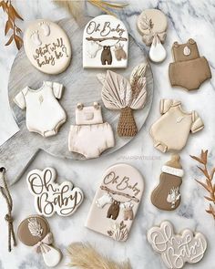 baby shower cookies are arranged on a marble platter with feathers and dried leaves in the background