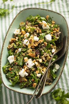 a green salad with feta cheese and walnuts in a blue bowl on a striped tablecloth