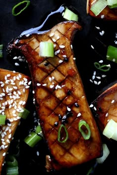 grilled pork chops with sesame seeds and green onions on a black surface next to sliced cucumbers