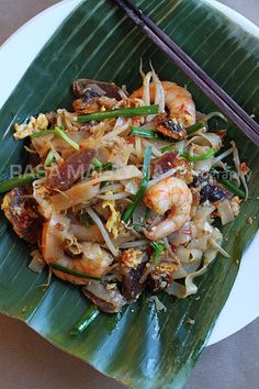 a white plate topped with food and chopsticks next to a green banana leaf