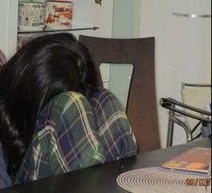 a woman sitting at a table with her head on the back of a chair looking down