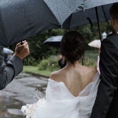 a bride and groom walking in the rain under umbrellas