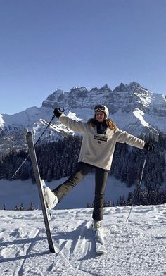 a woman standing on top of a snow covered slope holding her skis and poles