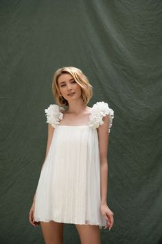 a woman in a short white dress posing for the camera with her hand on her hip