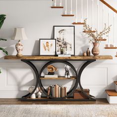 a table with books, vases and pictures on it in front of a staircase