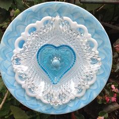 a blue and white plate with a heart shaped glass decoration on the center, surrounded by flowers