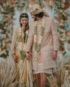 two people standing next to each other in front of flowers and greenery on the ground