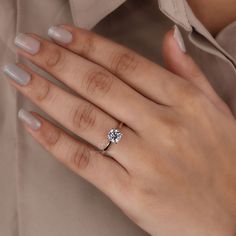 a woman's hand with a diamond ring on her left hand, wearing a beige shirt