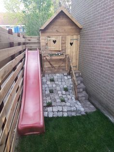 a small backyard with a red slide in the grass and a wooden shed behind it