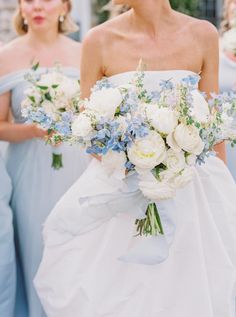 two bridesmaids in blue dresses hold bouquets of white and blue flowers as they walk down the aisle