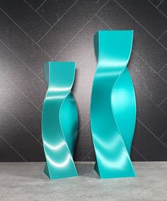 two blue vases sitting next to each other on top of a cement floor in front of a black wall