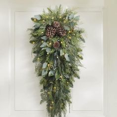 a wreath hanging on the front door with pine cones and greenery attached to it