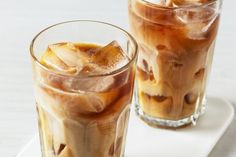 two glasses filled with iced coffee on top of a white plate