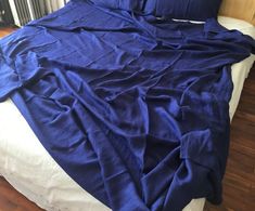 an unmade bed with blue sheets on top of it in a room that has wooden floors