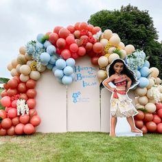 a woman standing in front of a birthday arch with balloons and flowers on the top