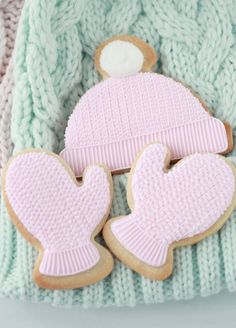 two knitted mittens and one cookie are laying on top of each other in front of a sweater