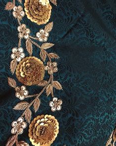 an embroidered fabric with gold flowers and leaves on green background, closeup view from the neck down