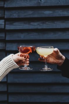 two people toasting with wine glasses in front of a black wall and wooden planks