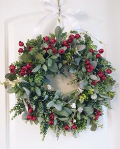 a wreath with red berries and greenery hanging on a door