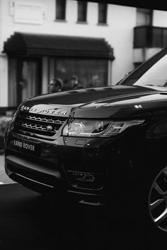 a black range rover parked in front of a white building with people walking by it