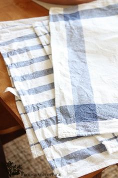 two blue and white checkered tea towels on a wooden table with a potted plant in the background