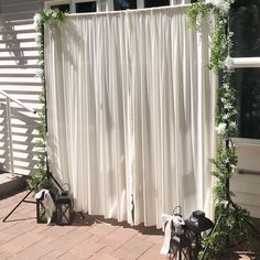 an outdoor wedding ceremony with white drapes and greenery on the side of the building