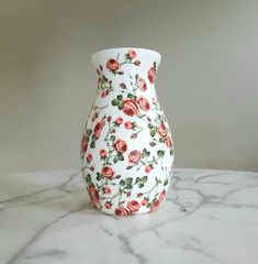 a white vase with red roses on it sitting on a marble table top next to a gray wall