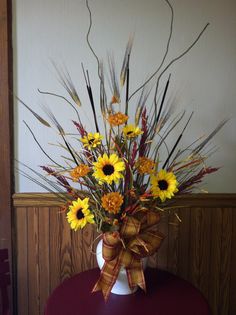 a vase filled with yellow and orange flowers on top of a red table next to a wall