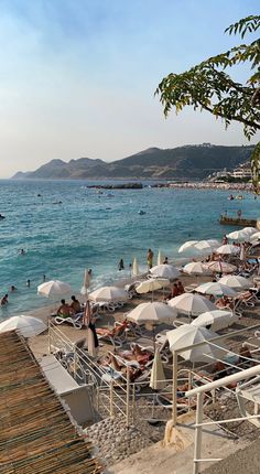 many people are on the beach with umbrellas and lounge chairs in the sand near the water