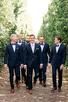 a group of men in suits and bow ties walking down a dirt road next to trees