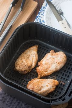 three pieces of chicken are cooking in a black pan on a table with utensils