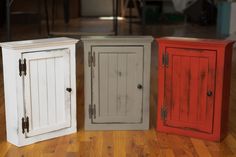 three different colored cupboards sitting on top of a wooden floor next to each other