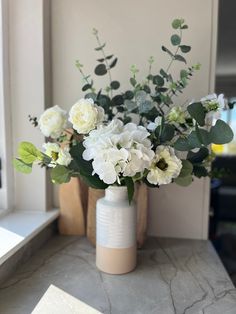 a vase filled with white flowers sitting on top of a counter next to a window