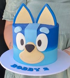 a person holding a cake in the shape of a dog's head on a plate