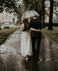 a man and woman walking down a rain soaked road holding an umbrella over their heads