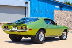 a green muscle car parked in front of a blue building with a sign on it