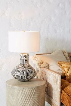 a lamp sitting on top of a wooden table next to a chair and ottoman covered in pillows