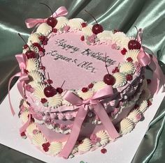 a heart shaped birthday cake with cherries and ribbons on it's side, sitting on top of a card