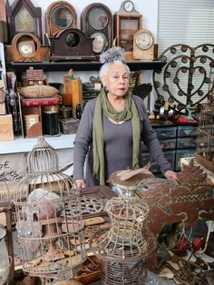 an older woman is standing in front of many birdcages and other antique items